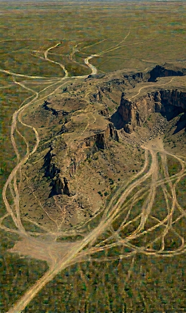 Aerial view of dirt trails converging around a steep desert canyon, unable to cross the cliff barrier
